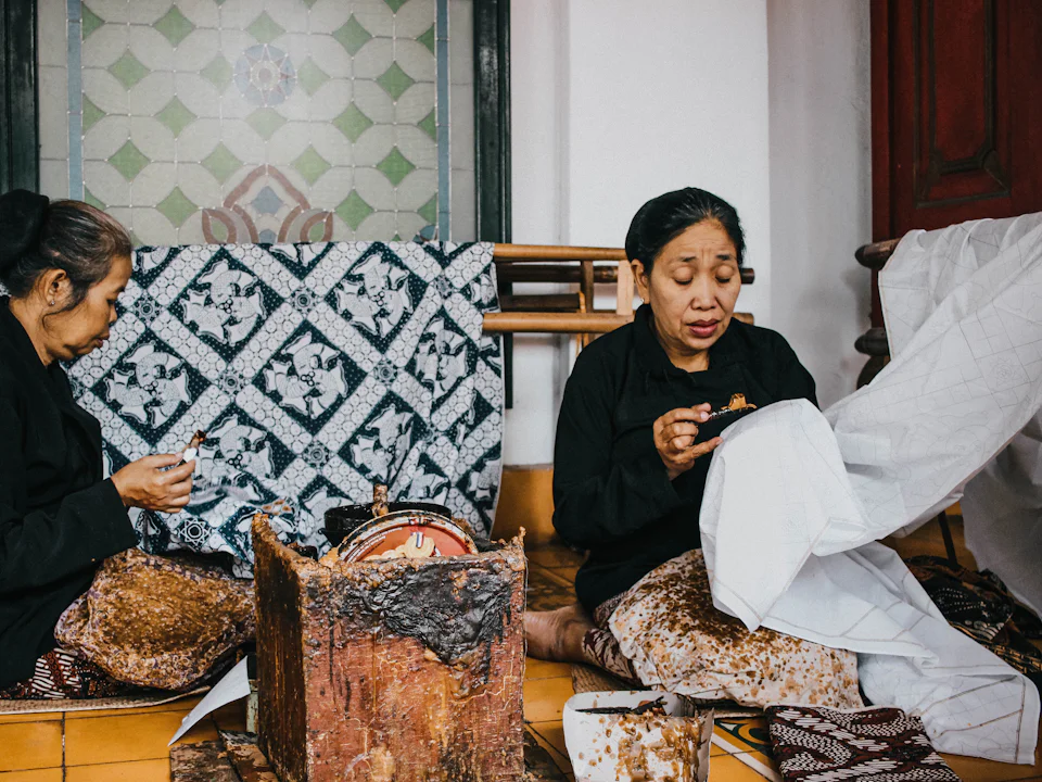 Two women in black drawing wax onto batik cloth with canting pens at the Keraton Yogyakarta
